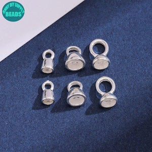 May include: Six silver-toned metal bell-shaped cord ends arranged in two rows of three, each featuring a circular loop at the top and a hollow opening at the base. The components vary in size, with a smooth, reflective finish throughout.