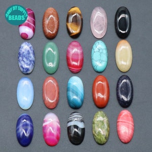 Pu&ograve; includere: Assortimento di 18 cabochon ovali in pietre preziose di vari colori e motivi, tra cui blu, verde, rosso, rosa, marrone, nero e bianco. I cabochon sono disposti in una griglia su una superficie grigia.