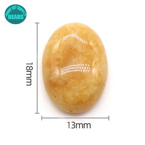 May include: A smooth, oval-shaped, yellow gemstone with a light brown hue. It measures approximately 1.8 inches in length and 1.3 inches in width.