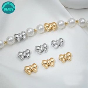 Könnte beinhalten: Eine Sammlung von goldenen und silbernen Perlen in Form von Schleifen. Die Perlen sind klein und haben ein zartes Design. Sie sind perfekt, um Schmuck oder Bastelarbeiten einen Hauch von Eleganz zu verleihen.