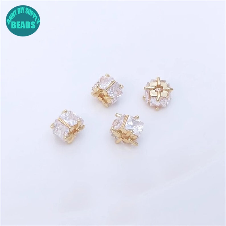 May include: Four gold-toned square-shaped beads with clear cubic zirconia stones. The beads are about 1/2 inch in size.