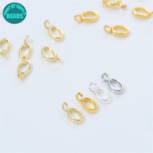 Könnte beinhalten: Eine Auswahl an gold- und silberfarbenen, oval geformten Schmuckverschlüssen mit einer kleinen Schlaufe oben. Sie sind auf einer weißen Oberfläche verstreut. Das Bild enthält auch einen türkisfarbenen Kreis mit dem Text "ANNY DIY SUPPLY BEADS".