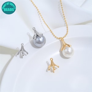 Puede incluir: Un collar de cadena de bolas doradas con un colgante de perla blanca que tiene una tapa metálica en forma de garra. Se incluyen dos tapas metálicas adicionales en forma de garra en tonos plata y oro, y una perla gris con tapa plateada.
