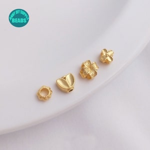 May include: Five gold-colored metal beads with different designs. The beads are arranged in a row on a white surface. The beads are all small and delicate, and they would be perfect for making jewelry or other crafts.