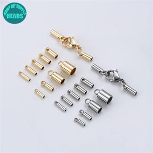 Op de afbeelding: Assortiment van gouden en zilveren metalen eindkappen en connectorgespen voor het maken van sieraden. De eindkappen zijn cilindrisch en hebben een kleine lus aan de bovenkant. De connectorgespen hebben een lang, recht gedeelte met een lus aan elk uiteinde en een karabijnhaak in het midden.