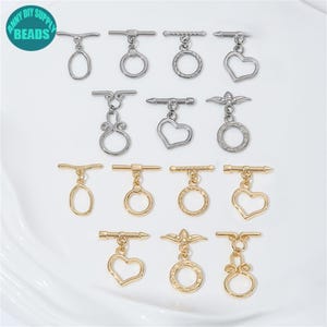 May include: A selection of toggle clasps in silver and gold. The clasps have diverse designs, such as oval, round, heart, and decorative forms. The image includes the text "ANNY DIY SUPPLY BEADS".