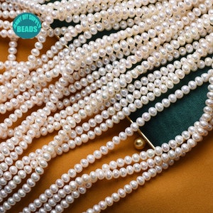 May include: A close-up of a strand of white freshwater pearls. The pearls are round and smooth, and they are arranged in a loose, flowing pattern. The pearls are on a brown and green surface.
