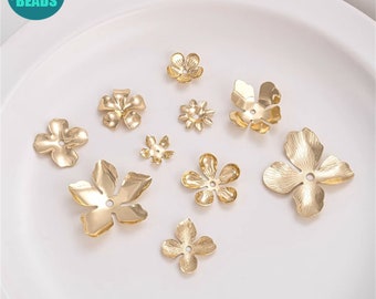 May include: A collection of gold-colored metal flower-shaped beads in various sizes. The beads have a matte finish and a hole in the center for stringing. The image is taken on a white surface.