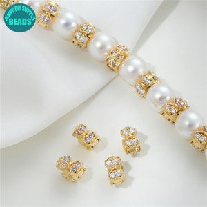 May include: Gold-tone butterfly-shaped bead spacers with clear and pink rhinestones. The spacers are shown with white pearl beads.