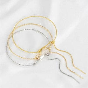 Könnte beinhalten: Drei goldene und silberne Kettenarmbänder mit verschiebbaren Perlen. Die Armbänder haben ein zartes, gedrehtes Kettenmuster.