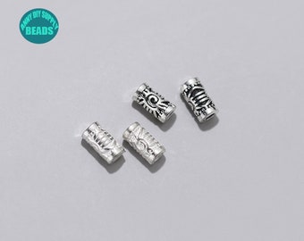 May include: Four silver metal beads with intricate designs. The beads are cylindrical and have a smooth, polished finish.