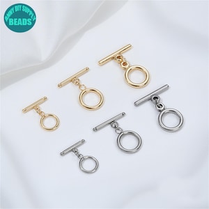 以下が含まれることがあります： 金と銀色のトーンのトグルクラスプの品揃え。これらのクラスプは、ジュエリー作りに最適で、バーとリングのデザインが特徴です。画像には、ターコイズの円の中に「ANNY DIY SUPPLY BEADS」というテキストが含まれています。