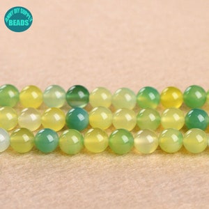 May include: A strand of green and yellow agate beads. The beads are round and smooth, and they are arranged in a graduated pattern, with the green beads at one end and the yellow beads at the other.