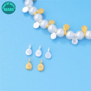 May include: A collection of jewelry-making supplies, including silver and gold-colored teardrop-shaped pendants and a beaded necklace with white pearls and gold accents. The image is set against a light blue background, with the text "ANNY DIY SUPPLY BEADS" in a circle.
