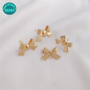 May include: Four gold-toned bow-shaped earring findings with a loop at the bottom. The findings are on a white surface.
