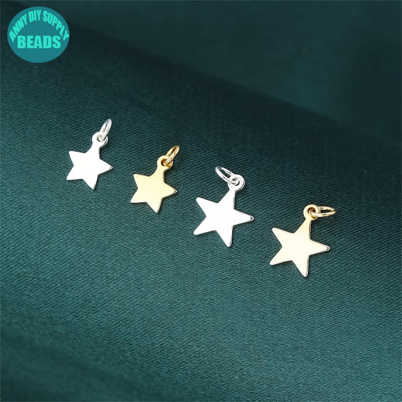 May include: Five silver and gold star-shaped charms with jump rings. The charms are arranged in a row on a green surface.