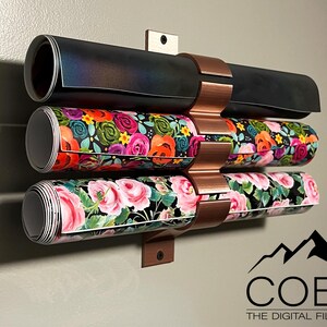 May include: A copper wall mount with three rolls of patterned paper. The paper is rolled and held in place by the mount. The mount is attached to a wall. The text "COBO THE DIGITAL FILE SHOP" is visible at the bottom of the image.