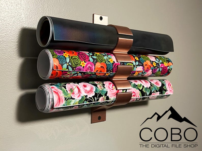 May include: A copper wall mount with three rolls of patterned paper. The paper is rolled and held in place by the mount. The mount is attached to a wall. The text "COBO THE DIGITAL FILE SHOP" is visible at the bottom of the image.