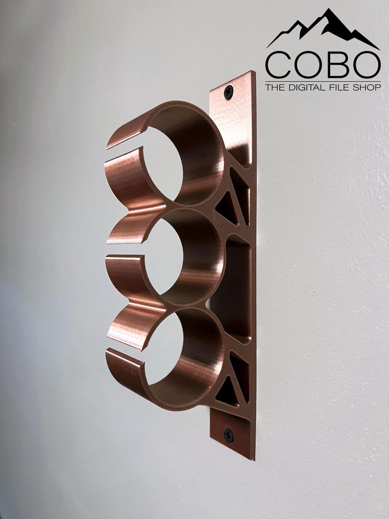 May include: A copper-colored metal wall mount with three circular openings for holding items. The mount is attached to a white wall with screws. The text "COBO THE DIGITAL FILE SHOP" is visible in the upper right corner of the image.