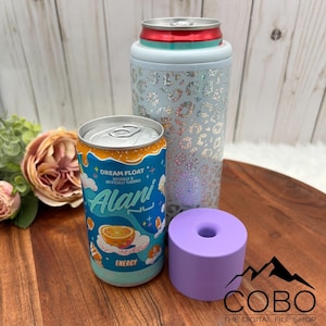 May include: An Alani Nu Dream Float energy drink can next to a light blue leopard print can cooler and a small purple cylindrical object. The Alani can is blue and orange with the words "Dream Float" and "Alani" printed on it.