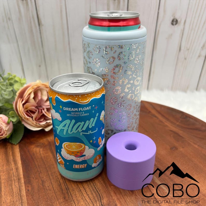 May include: An Alani Nu Dream Float energy drink can next to a light blue leopard print can cooler and a small purple cylindrical object. The Alani can is blue and orange with the words "Dream Float" and "Alani" printed on it.