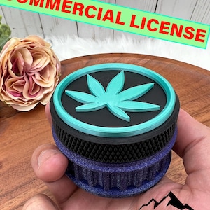 May include: A 3D printed grinder with a black base, a teal top featuring a green marijuana leaf design, and a blue and black textured bottom. The grinder is being held in a hand.