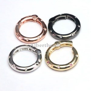 May include: Four metal ring clasps with a decorative design of small stars and a single larger star. The rings are available in silver, gold, rose gold, and black.
