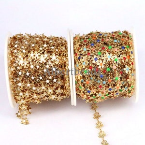 May include: Two spools of gold-colored metal chain with flower-shaped links. One spool has plain gold flowers, the other has flowers with colorful enamel centers.