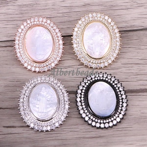 May include: Four oval-shaped pendants with religious imagery. Each pendant features a central design surrounded by a ring of clear, sparkling stones. The frames are in rose gold, gold, silver, and black.