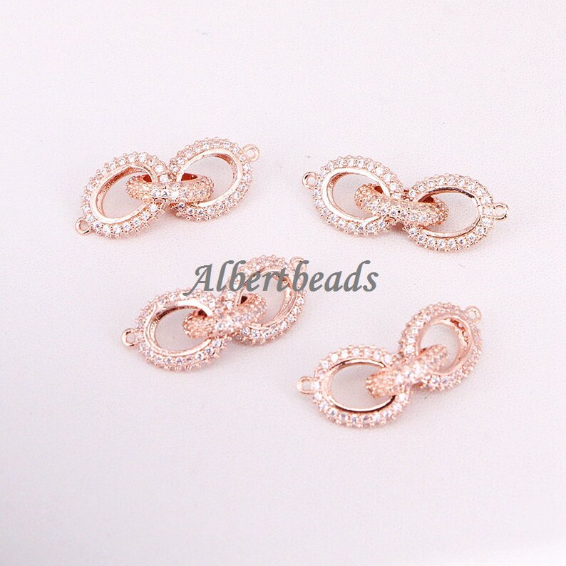 May include: Four rose gold infinity charm connectors with clear cubic zirconia stones. The connectors are designed to be used in jewelry making.