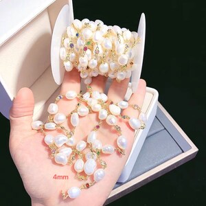May include: A white pearl and gold chain with colorful gemstones. The chain is wound around a spool and a section of the chain is laid out on a white surface. The pearls are 4mm in size.
