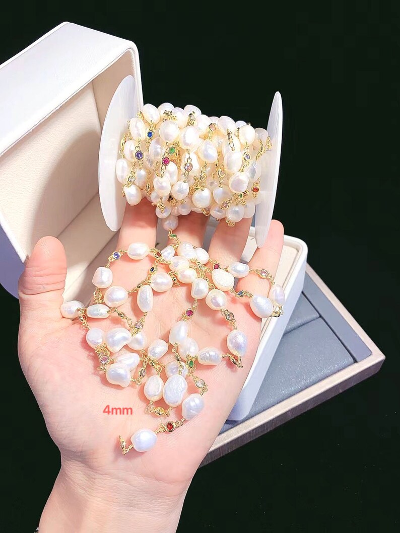 May include: A white pearl and gold chain with colorful gemstones. The chain is wound around a spool and a section of the chain is laid out on a white surface. The pearls are 4mm in size.