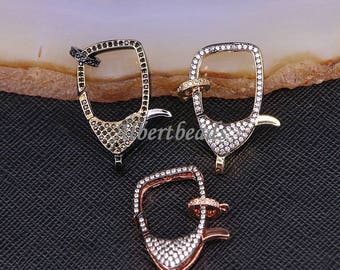 May include: Three silver, gold, and rose gold tone lobster clasps with clear and black cubic zirconia stones. The clasps are square shaped with a rounded edge.