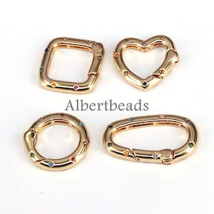 May include: Four gold-toned metal clasps with colorful gemstone accents. The clasps are in the shapes of a square, heart, oval, and circle.