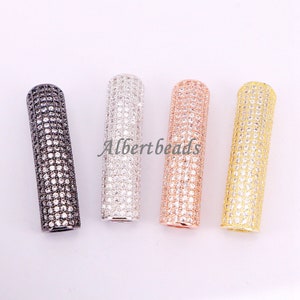 May include: Four cylindrical beads with a pave setting of clear cubic zirconia stones. The beads are in black, silver, rose gold, and gold.