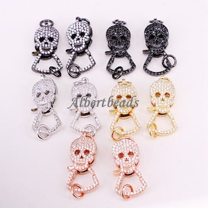 May include: Eight skull-shaped clasps with clear cubic zirconia stones. The clasps are in different metal finishes: silver, gold, rose gold, and black.