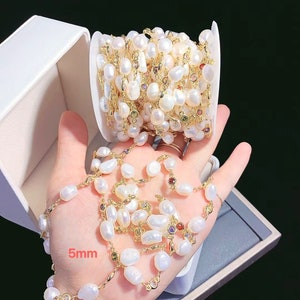 May include: A white pearl and gold chain with colorful gemstones. The chain is wound around a spool and is also laid out in a straight line. The pearls are 5mm in size.