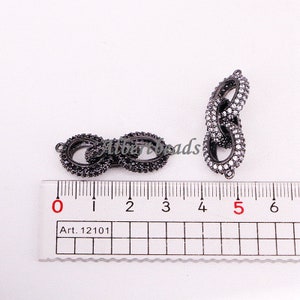 May include: Two black metal connector charms with clear cubic zirconia stones. The charms are 5 cm long and are shown on a ruler.
