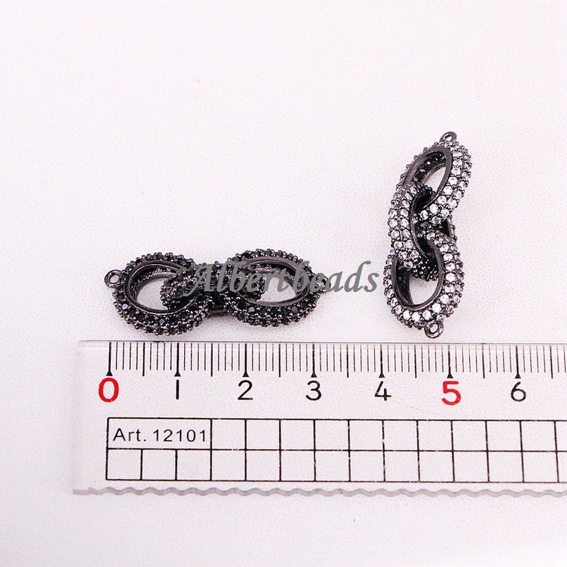May include: Two black metal connector charms with clear cubic zirconia stones. The charms are 5 cm long and are shown on a ruler.