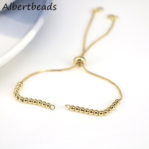 May include: A gold-toned adjustable bracelet with a beaded chain and a sliding knot closure. The bracelet is made of metal.