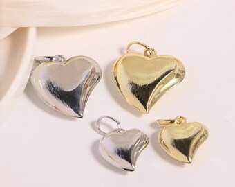 May include: Four heart-shaped pendants, two gold and two silver, with a brushed finish. The pendants are all the same size and shape, and they are hanging from a white surface.