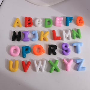 Peut inclure: Un ensemble de lettres de l'alphabet colorées et brillantes, disposées en rangées. Chaque lettre est d'une couleur différente, notamment jaune, rouge, blanc, vert, rose, bleu, orange, noir, violet et bleu clair. Les lettres sont dans une police arrondie et ludique.
