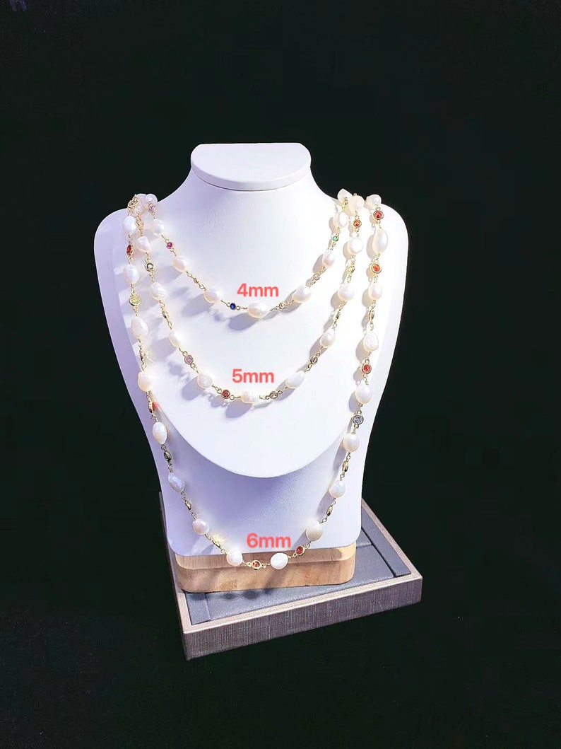 May include: Three pearl necklaces with different sized pearls, 4mm, 5mm, and 6mm, on a white mannequin. Each necklace has small colorful gemstones interspersed throughout.