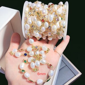 May include: A white pearl chain with gold accents and colorful gemstones. The chain is 6mm wide and is wound around a white box.