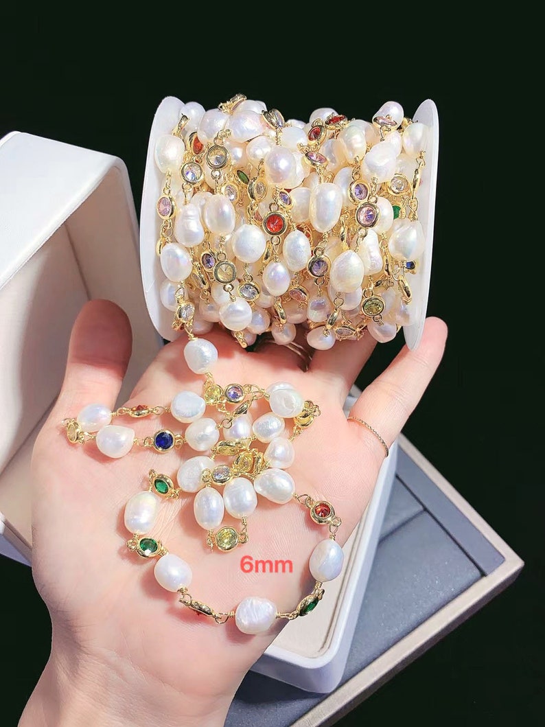 May include: A white pearl chain with gold accents and colorful gemstones. The chain is 6mm wide and is wound around a white box.