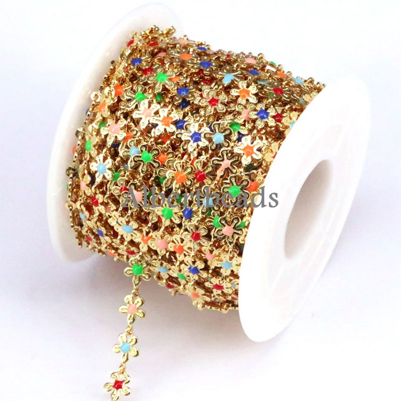 May include: A spool of gold-colored chain with colorful flower-shaped beads. The chain is made of metal and the beads are made of glass. The chain is on a white spool.