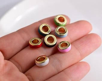 May include: A collection of colorful enamel beads with gold-colored rims. The beads are in various colors, including red, blue, green, pink, black, and white. These small, round beads are ideal for jewelry making and crafting projects.
