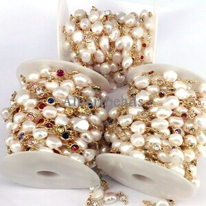 May include: A spool of white pearl and gold chain with colorful gemstone accents. The chain is wrapped around a white spool.