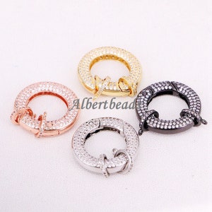 May include: Four round, silver-toned,  clasp-style jewelry connectors with clear crystal accents. The connectors are in gold, rose gold, silver, and black.