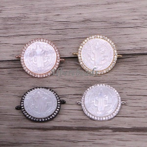 May include: Four oval-shaped pendants with a white mother of pearl center featuring a Saint Christopher image. Each pendant is surrounded by a circle of clear cubic zirconia stones and has a silver, gold, rose gold, or black finish.